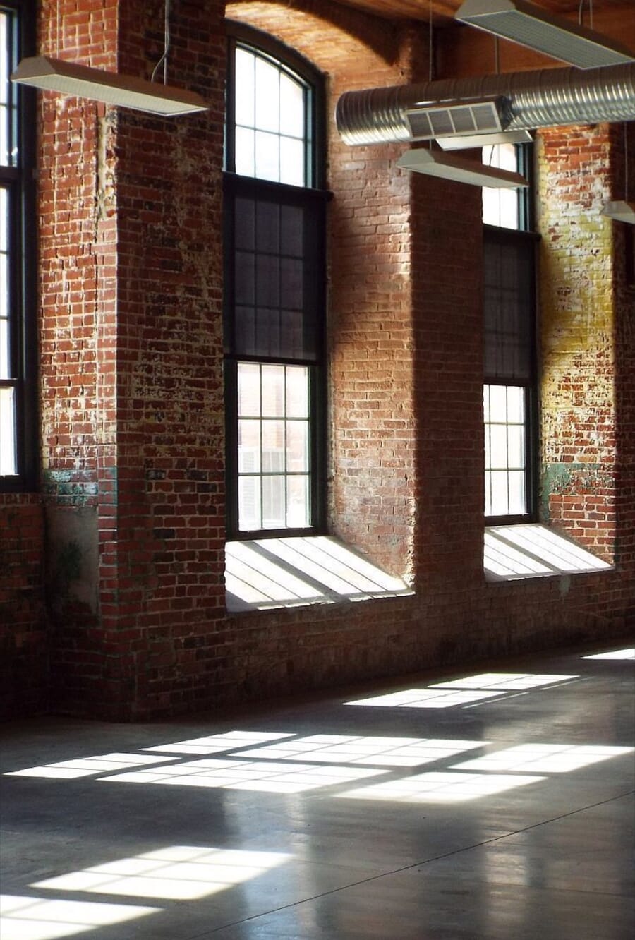 Sunlight through tall windows in an empty brick mill room