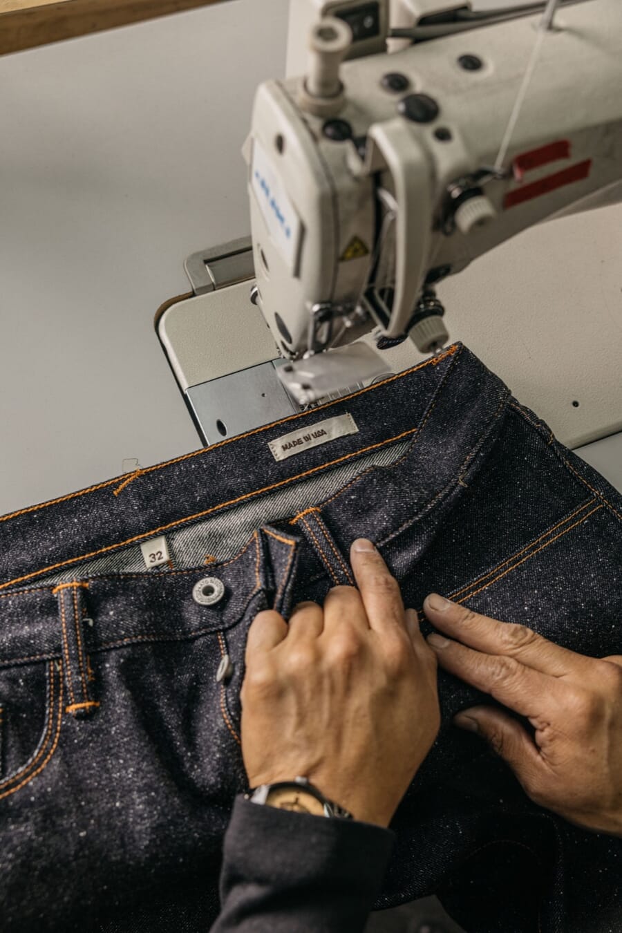 Hands guiding a raw denim waistband under a sewing machine