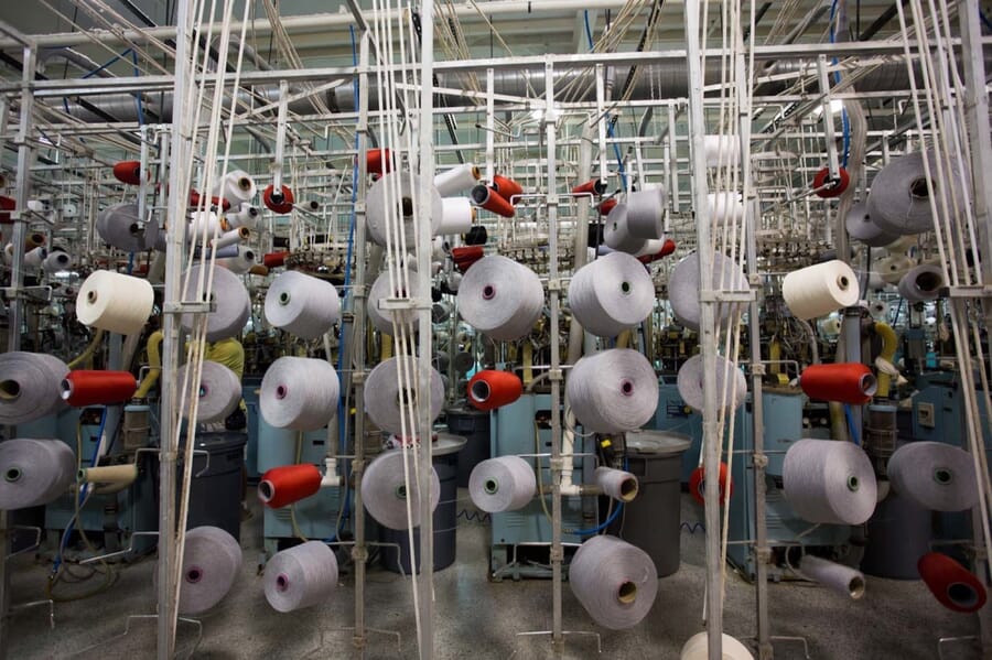 Yarn cones in red and white hanging above knitting machines