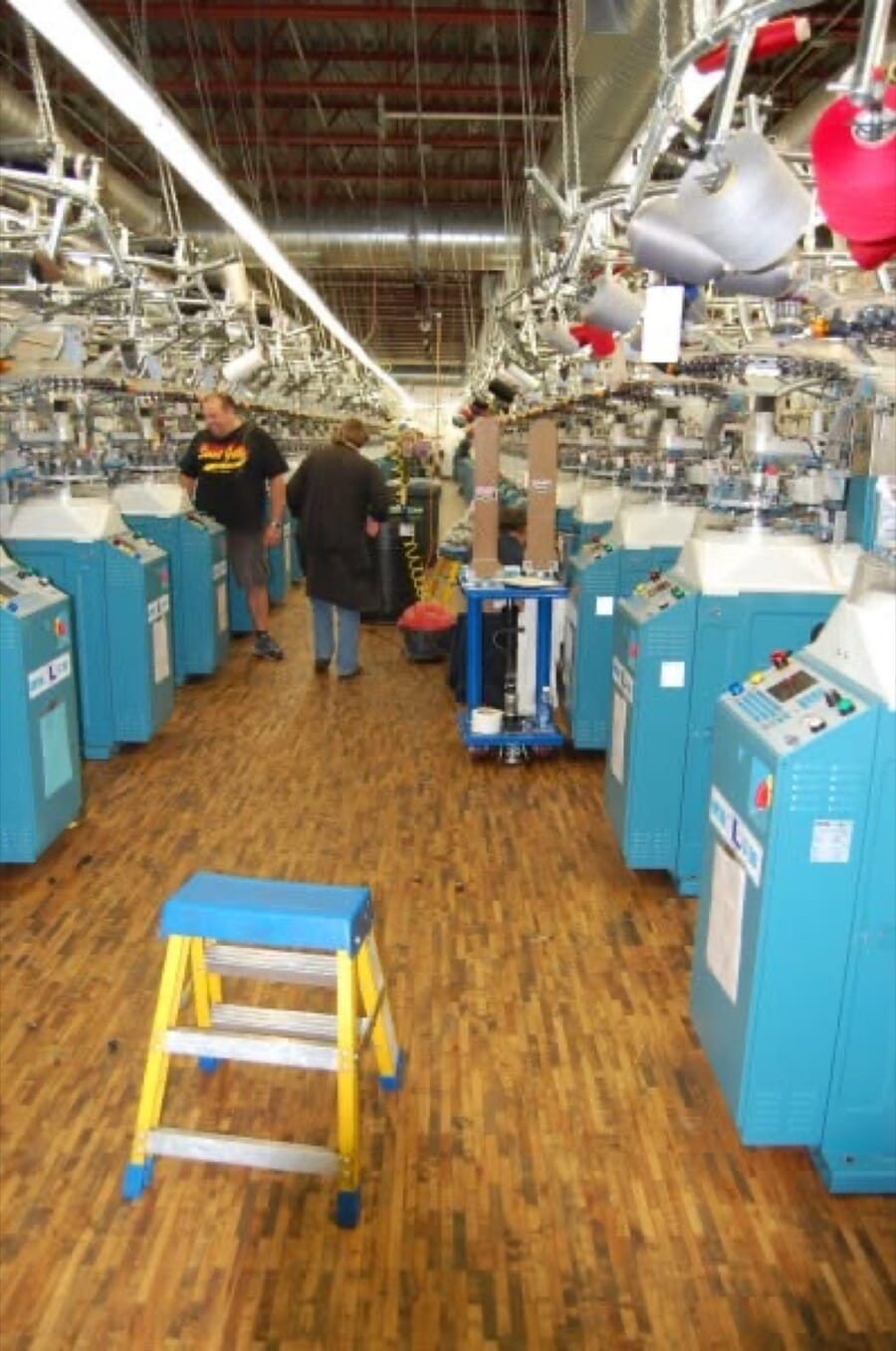 Aisle between rows of blue sock knitting machines with a step ladder