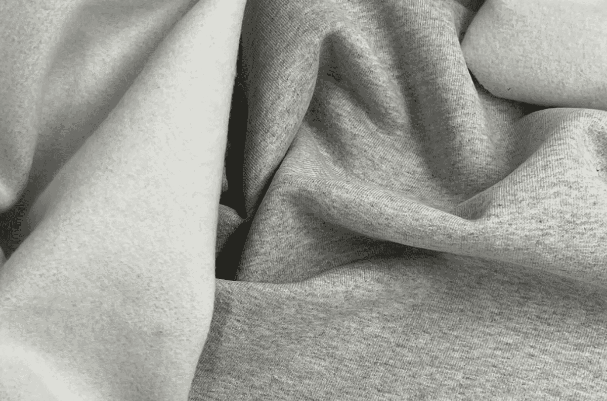 Close-up of grey fleece fabric folded to show both faces: the soft raised nap on the left and the flat knit face on the right.