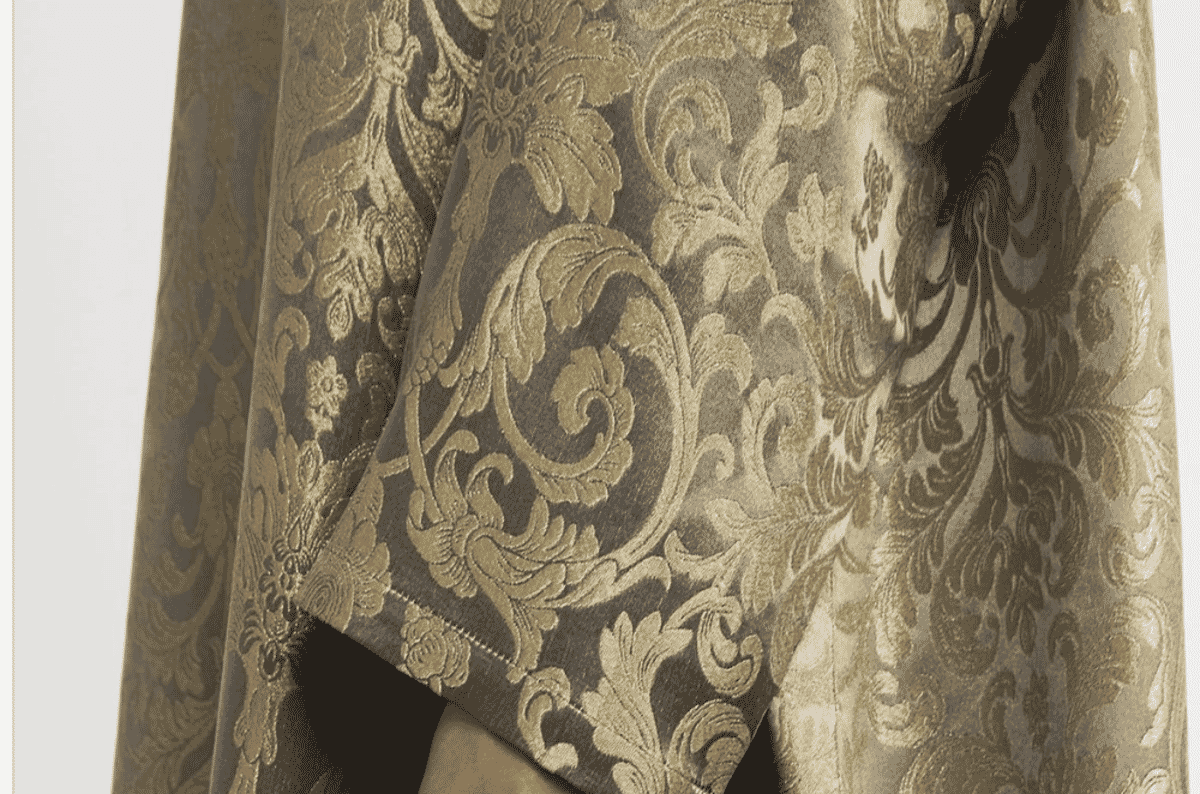 Detailed close-up of a woven jacquard fabric surface with raised botanical motifs in cream and gold tones, showing yarn floats characteristic of loom-woven figured cloth.