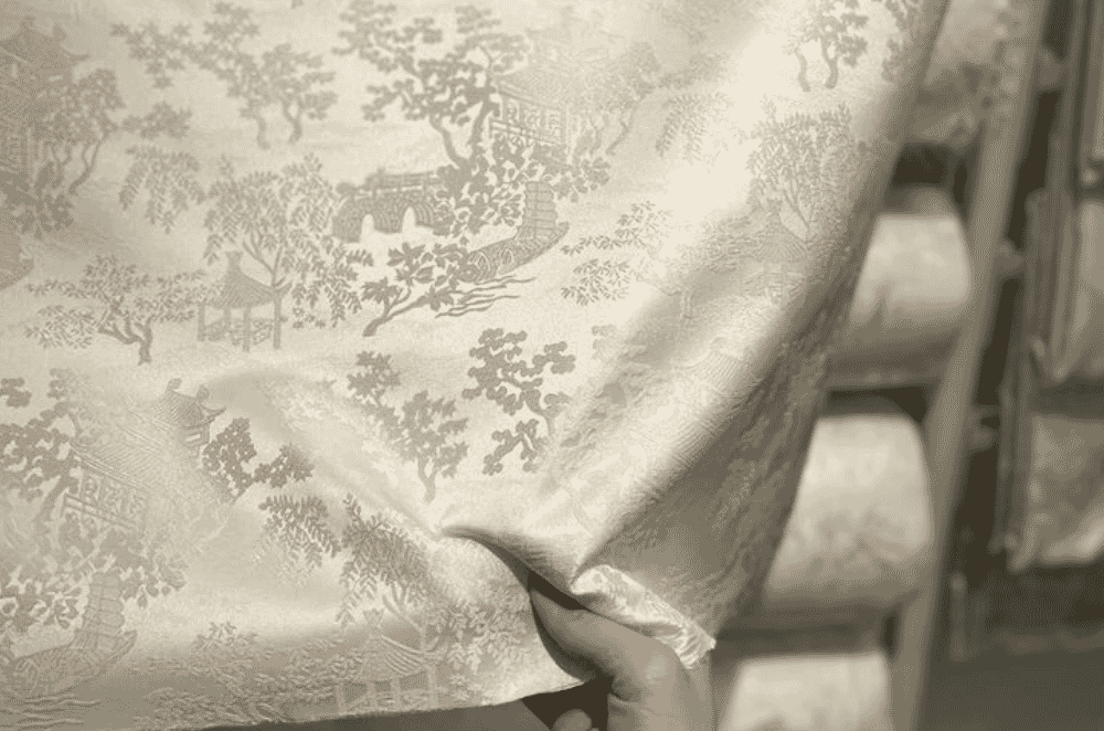 Ornate figured fabric pattern with dense multi-colour motifs typical of tapestry-style jacquard used in fashion outerwear and dresses.