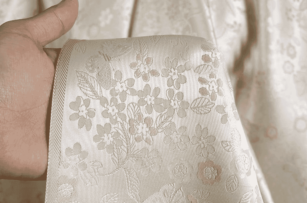 Heavyweight brocade fabric with a raised metallic-thread motif against a satin ground, typical of occasion coats and statement jackets.