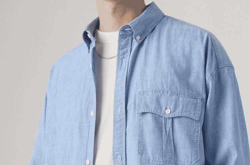 Close-up detail of a light blue chambray shirt showing the soft heathered surface produced by an indigo dyed warp and white undyed weft in a tight plain weave.