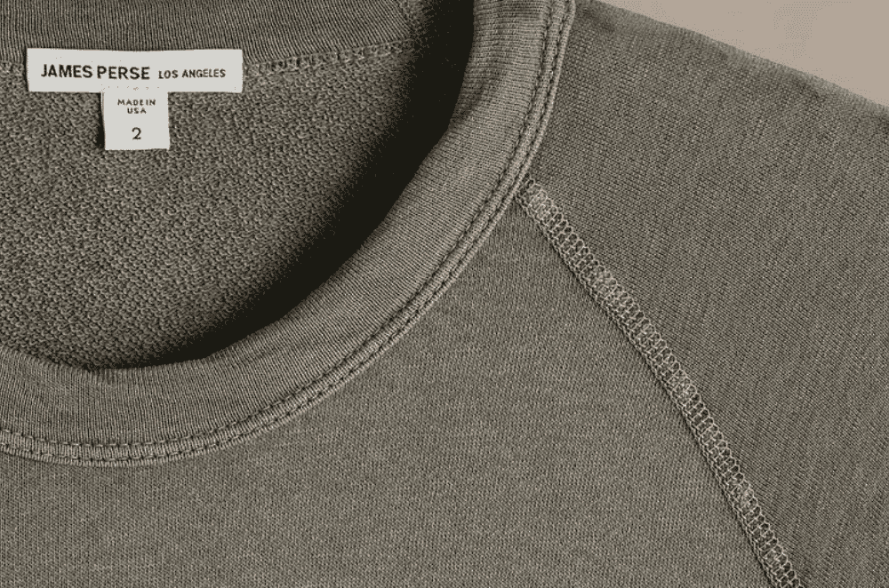 Rolls of knitted cotton fabric in earthy tones stacked on a factory shelf, showing the loop-back texture typical of French terry knits.