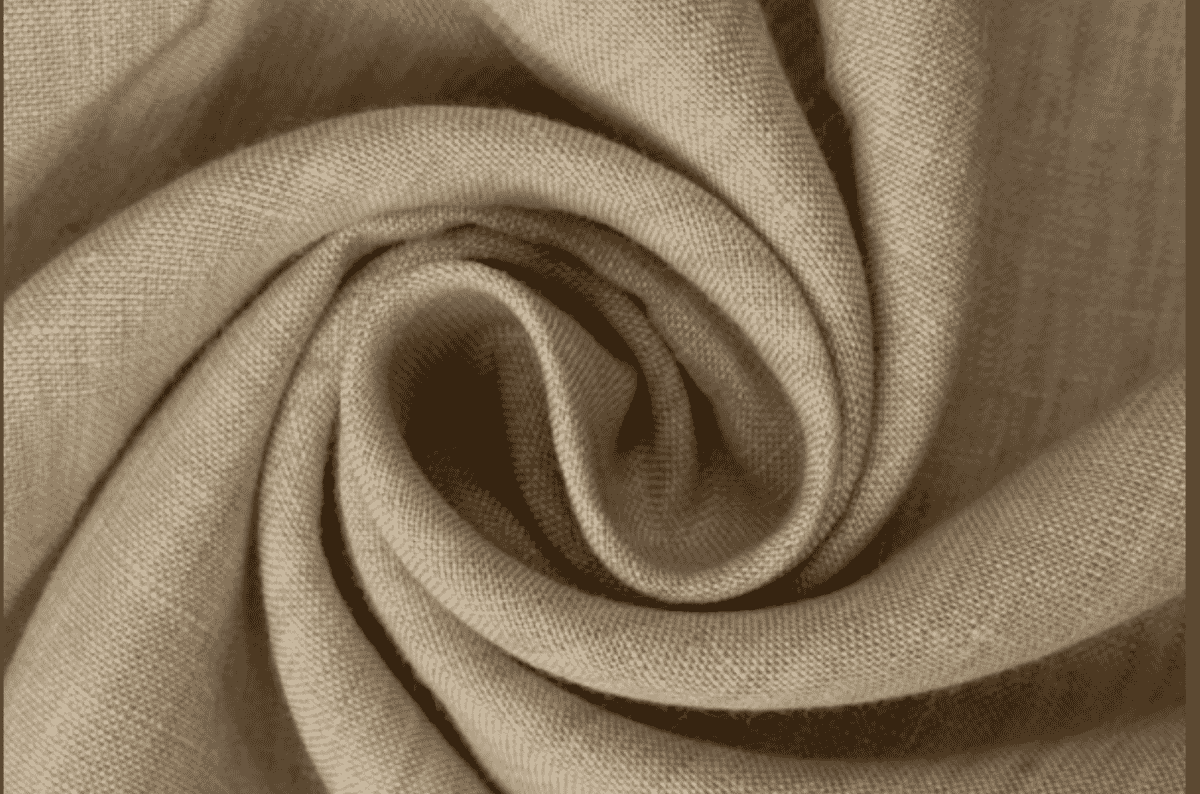 A length of natural-toned cloth swirled into a spiral to show how it falls, with a visible plain-weave grid and slubby irregular yarns.