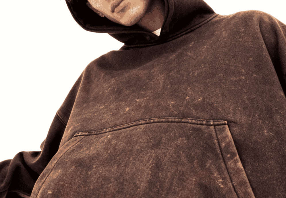 A washed grey hoodie hanging on an industrial rail with visible fade and marbled contrast, characteristic of an acid wash finish.