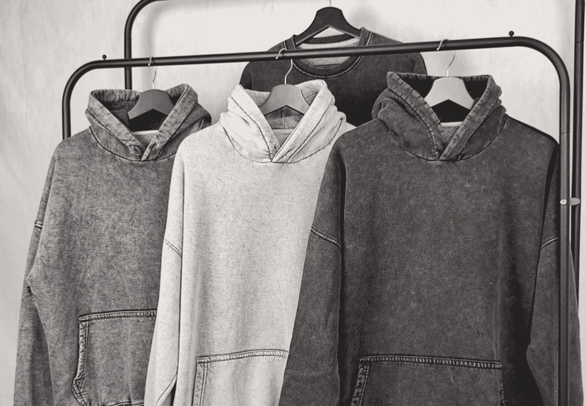 Three washed heavyweight hoodies hanging on a rail, the garment class most often specified by GSM.