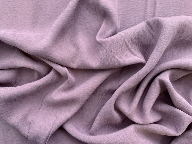 Rolls of drapey viscose fabric in soft neutral tones stacked at a Portuguese textile mill, showing the fluid hand characteristic of regenerated cellulose.