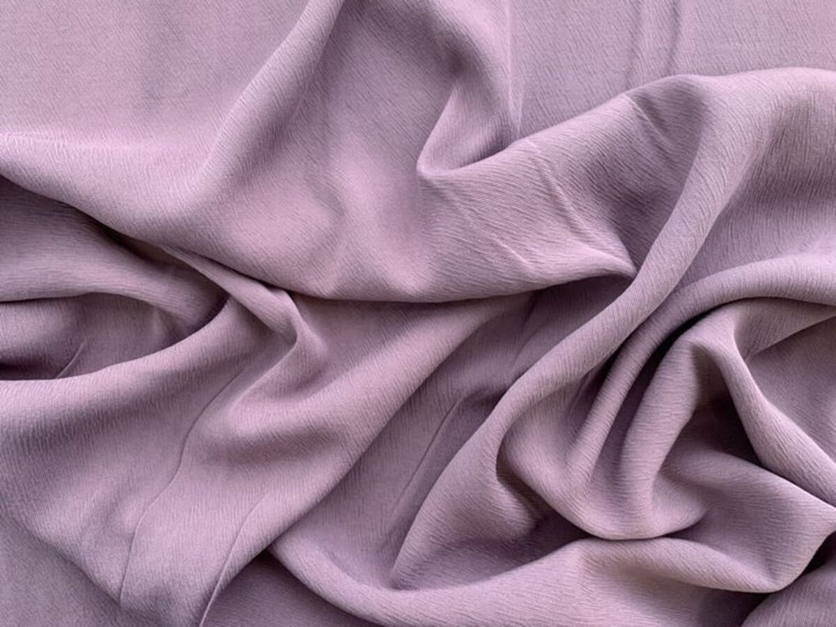 Soft mauve Tencel-viscose crepe fabric fallen into loose folds, showing the fine crinkled surface and fluid drape of a sueded crepe.