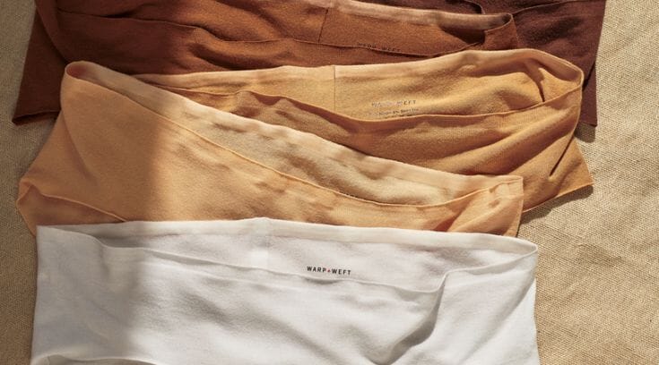 Close-up of soft cellulosic knit fabric folded on a Portuguese factory inspection table, showing the fine hand of micro-modal jersey used in premium underwear.