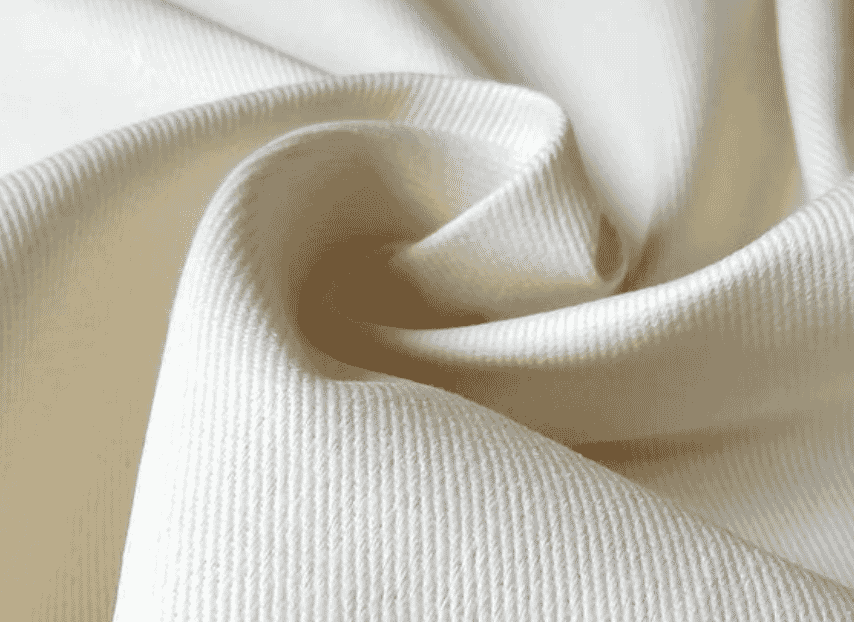 Rolos de sarja algodão penteado 240-500 g/m² em cores natural, khaki, navy e olive em fábrica Vale do Ave (Bragil, Solstício, Somelos) para produção chinos Officine Générale e workwear heritage.