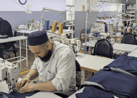 Machinist sewing indigo denim panels at a single-needle machine