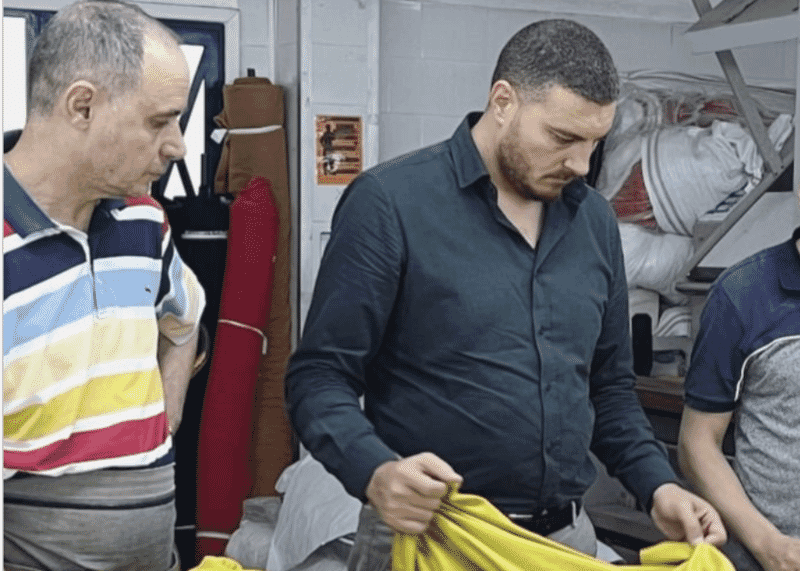 Two people reviewing a mustard garment at an inspection table