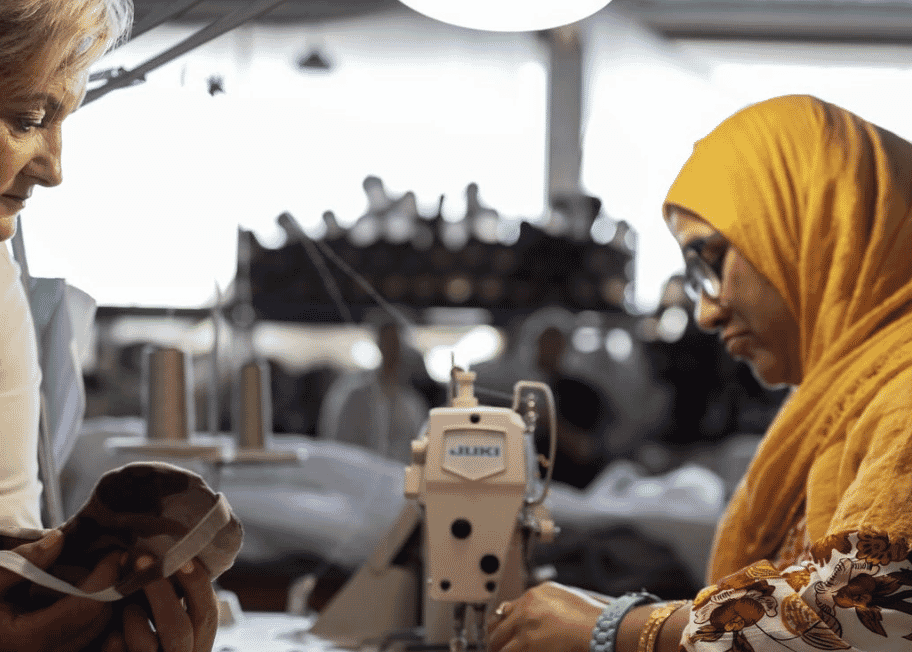 Machinist sewing at an industrial machine while a colleague holds up a fabric piece