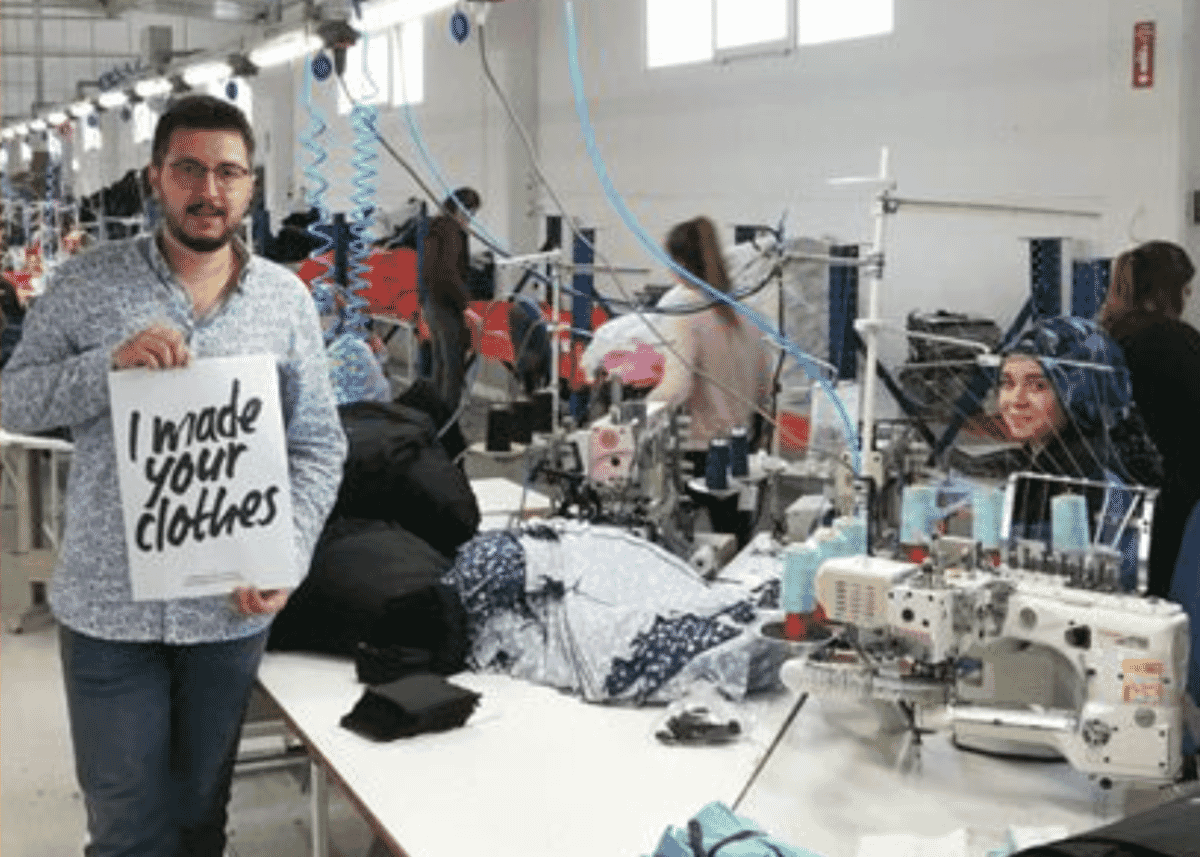 Worker holding an I made your clothes sign beside a sewing line