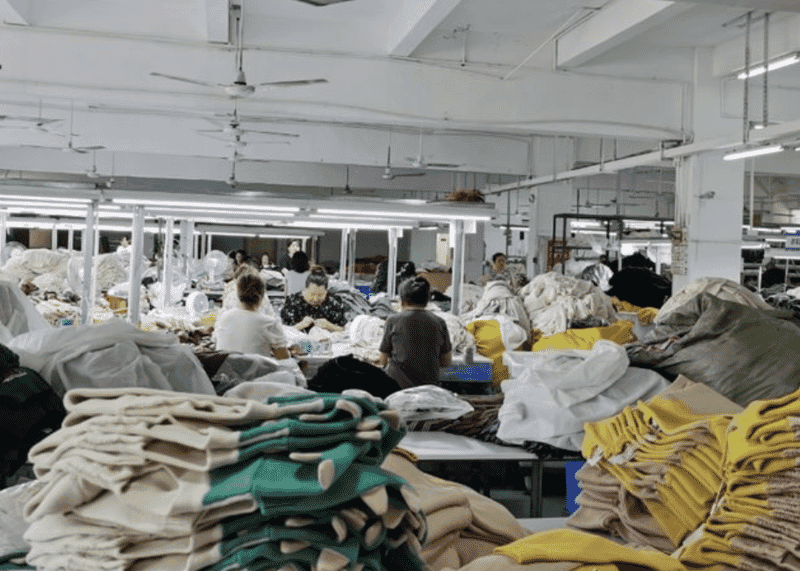 Stacks of green, cream and mustard knitwear between operations on a busy production floor