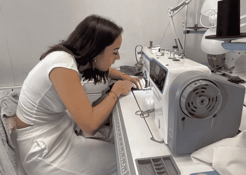 A machinist guiding fabric through an industrial sewing machine in a small production room